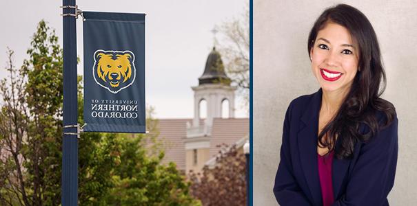 A photo of Campos-Spitze looking forward and smiling beside a banner with the UNC logo on it.